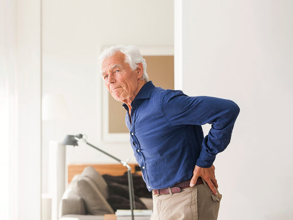 Ein Mann mit nicht-spezifischen Rückenschmerzen greift sich an den schmerzenden unteren Rücken.